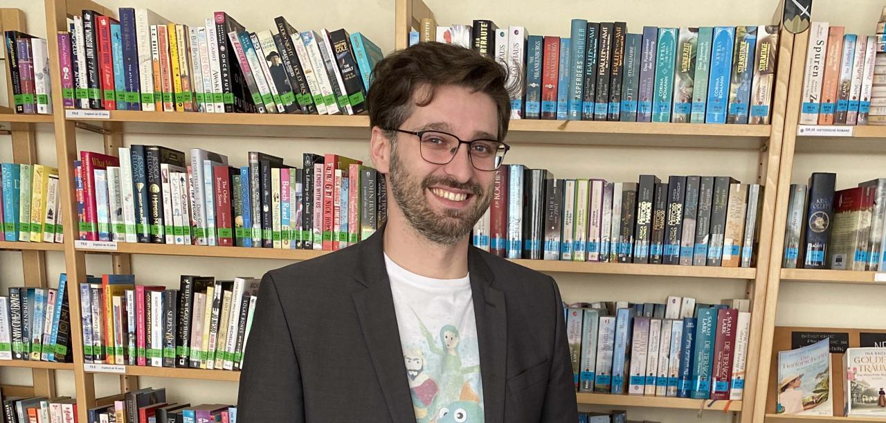Ein Mann steht hinter Werbeartikel, dahinter ein Bücherregal