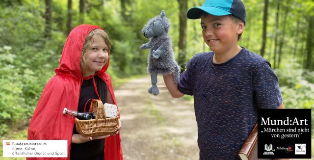 Ein Mädchen mit Rokäppchenumhang und eine Junge mit einer Wolfshandpuppe