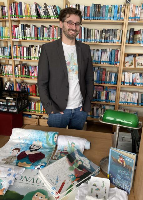 Ein Mann steht hinter Werbeartikel, dahinter ein Bücherregal