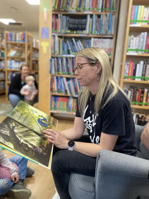 Ein Frau sitzt auf einem Sessel und liest ein Buch vor