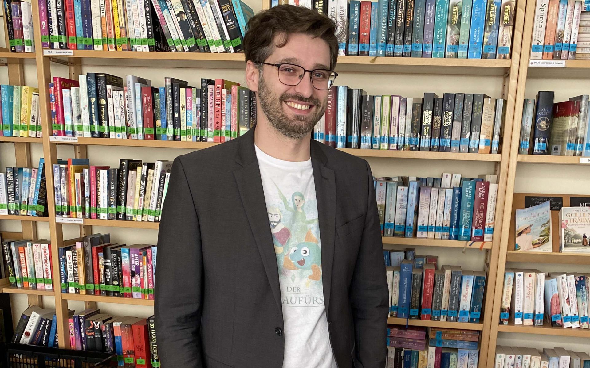 Ein Mann steht hinter Werbeartikel, dahinter ein Bücherregal