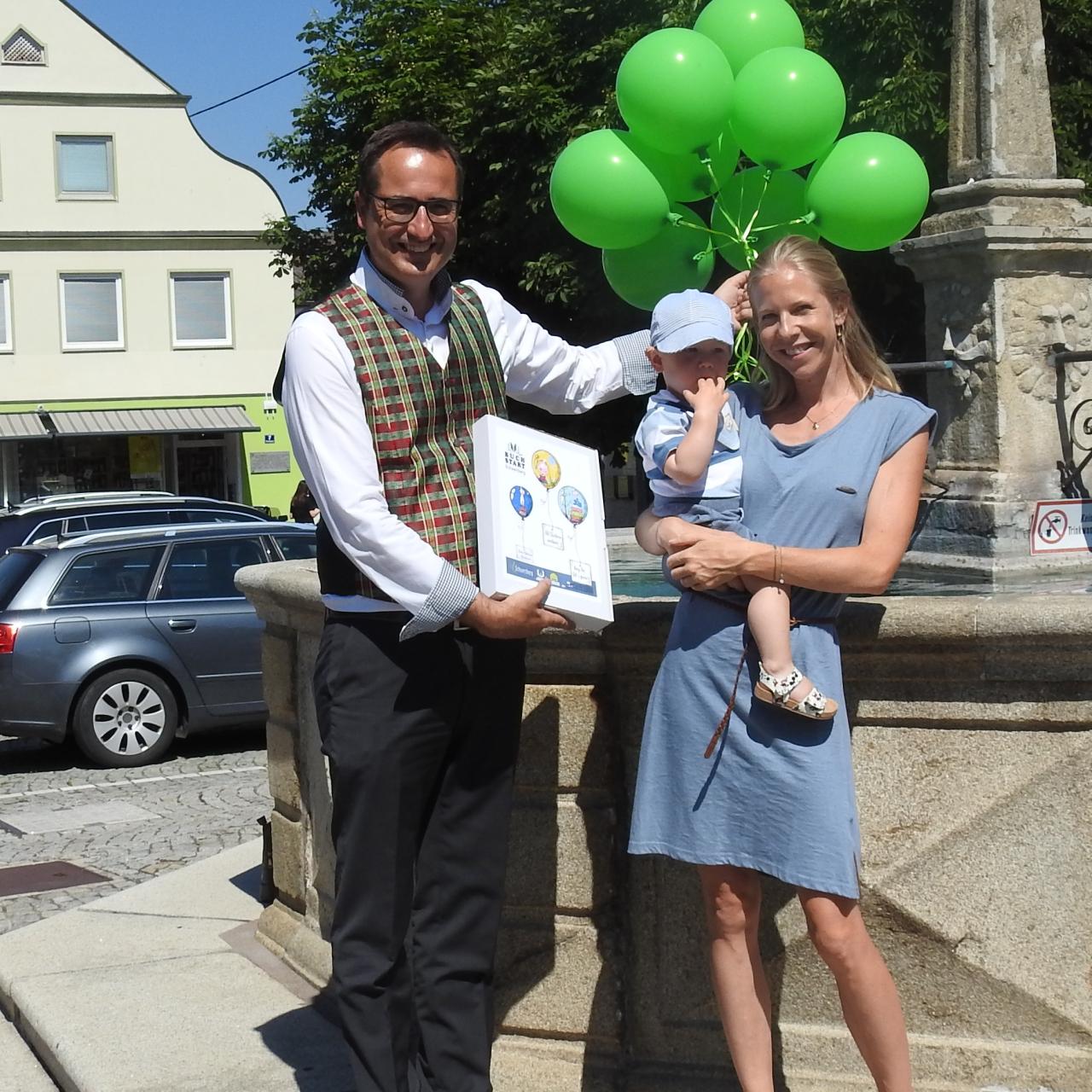 Bürgermeister mit Luftballons und einer Mama mit Kind