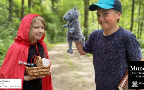 Ein Mädchen mit Rokäppchenumhang und eine Junge mit einer Wolfshandpuppe