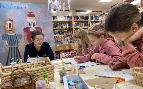 Ein Frau liest drei Kindern aus einem Buch vor
