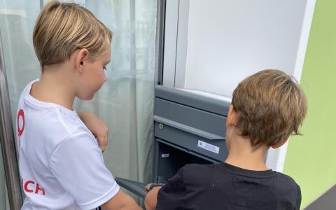 Zwei Kinder geben ihre Bücher in einem Postkasten zurück